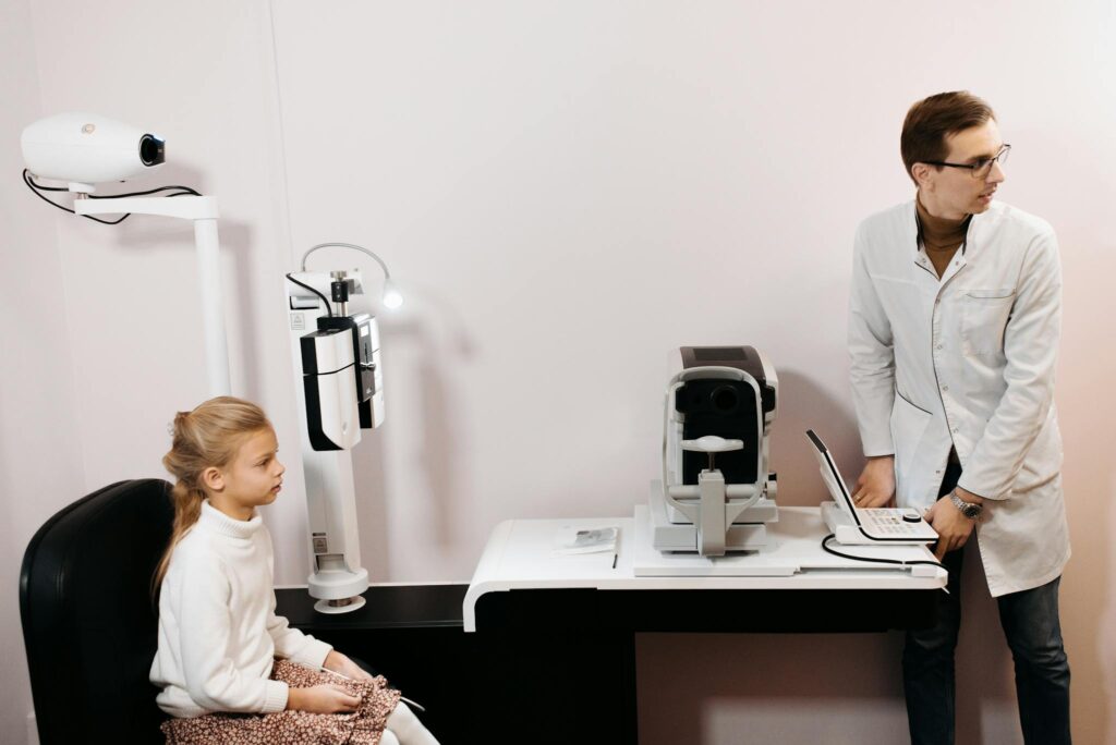 A young girl sits for an eye exam with an optometrist using digital equipment.