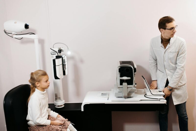 A young girl sits for an eye exam with an optometrist using digital equipment.